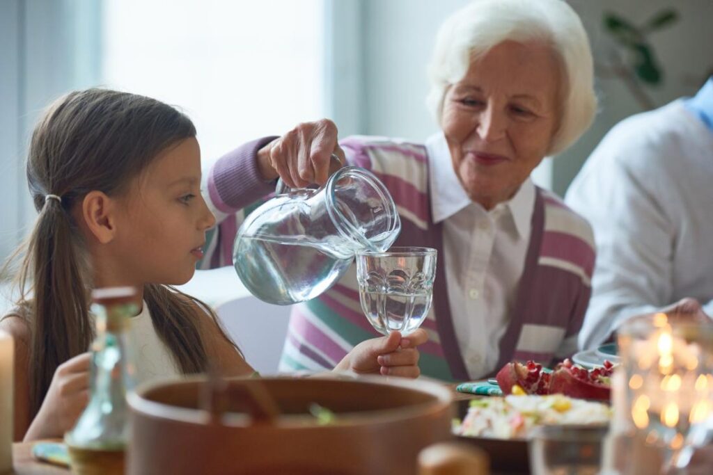 senior woman pouring water from jug at family meal into glass for young child Íme 21 etikett szabály, amint nemcsak a férfiaknak, de a nőknek is ismerni kell